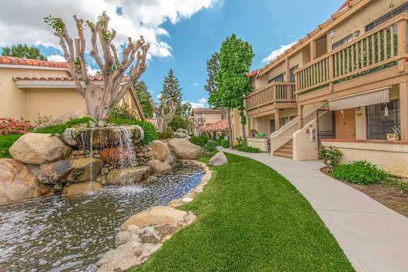 a waterfall flows into a pond in front of a building at Victoria Springs Apartments, California, 92504