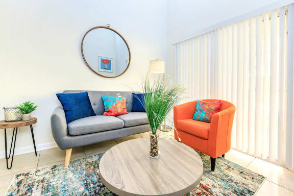 A living room with a grey couch, a small table, a round mirror, a potted plant, and a rug. at Saratoga Resort Villa Apartments, Kissimmee, FL, 34746