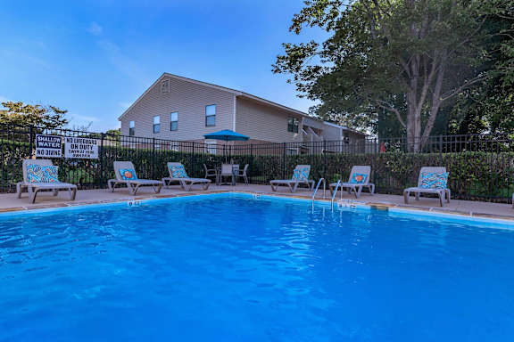 a swimming pool with chairs and a house in the background