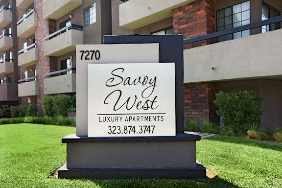 A sign for Savoy West Luxury Apartments is displayed in front of a building.