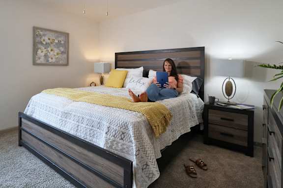 A woman is sitting on a bed with a yellow blanket and a white patterned bedspread.