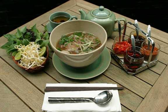 A table with a bowl of soup, a cup of tea, and some condiments.