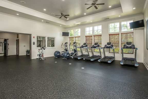 A spacious gym with treadmills, exercise bikes, and a ceiling fan.