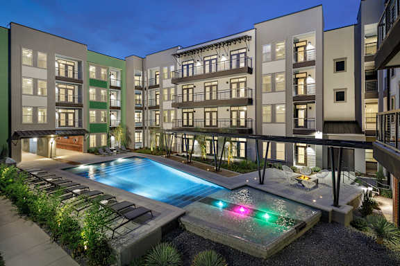 Resort-style courtyard pool with lounge seating, surrounding balconies, and evening lighting throughout the community