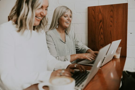 two women sitting at a table with a laptop