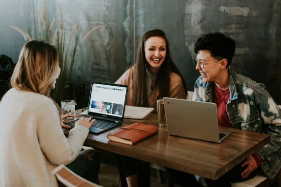 three people sitting at a table with laptops