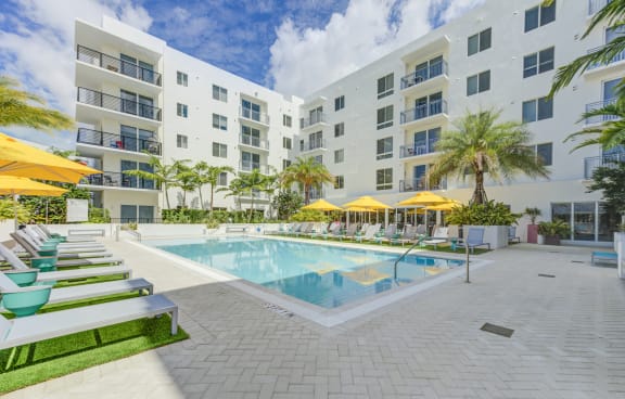 an outdoor swimming pool with lounge chairs and umbrellas in front of an apartment building