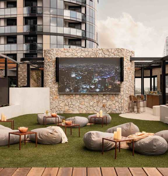 A modern outdoor seating area with bean bag chairs and a large screen on a stone wall.