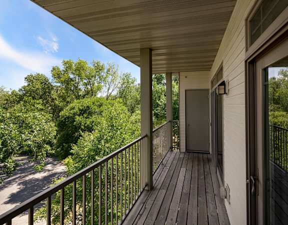 A balcony with a door and a window overlooking a tree-filled area.