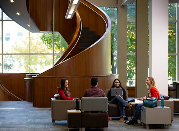 Four people sitting in a circle in a room with a spiral staircase.
