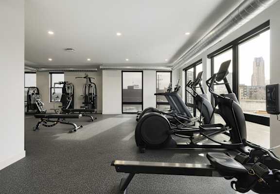 A gym with a row of treadmilers and elliptical machines.