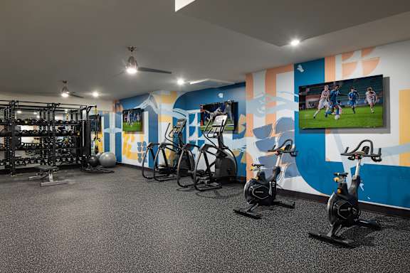 A gym with exercise bikes and a wall mural of a soccer game.
