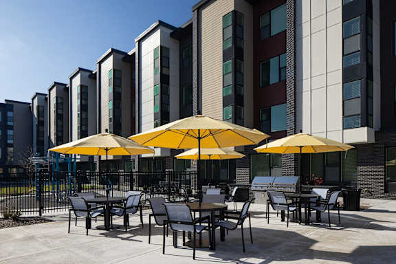 A patio with tables and chairs and umbrellas in front of a building.