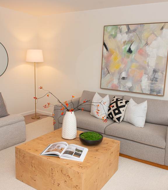 A living room with a grey couch, a wooden coffee table, and a painting on the wall.