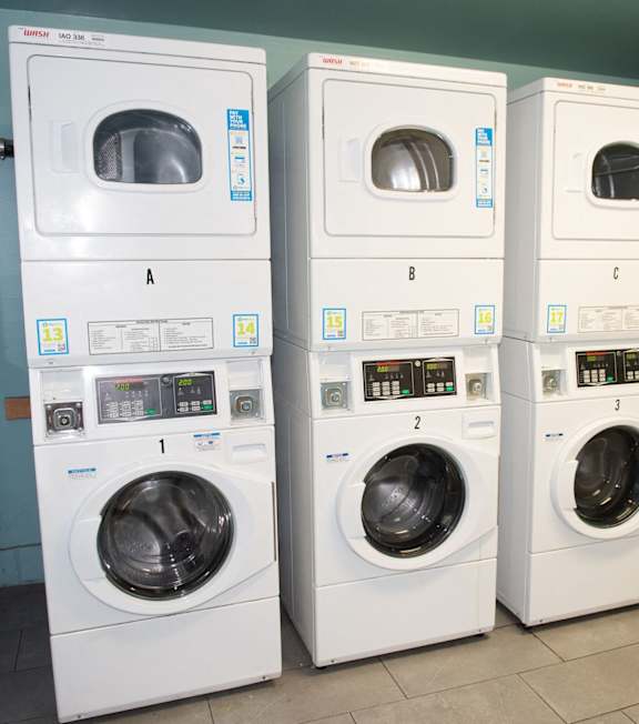 A row of white front loading washing machines are lined up in a laundromat.
