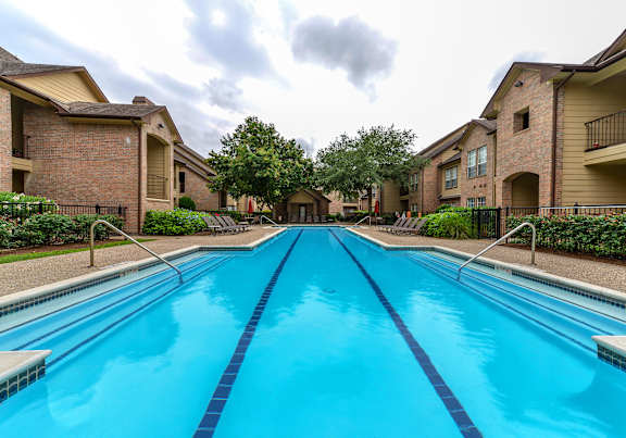 A long rectangular swimming pool in front of apartment buildings.