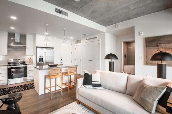 A modern living room with a kitchen area in the background.