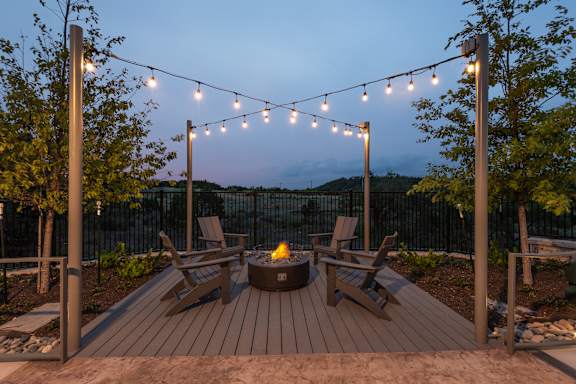 A backyard with a fire pit and chairs under string lights.