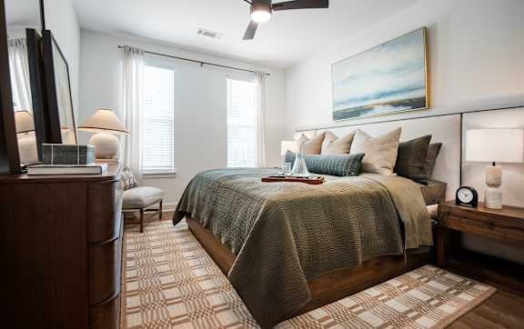A well-lit bedroom with a bed, a chair, a potted plant, and a fireplace.