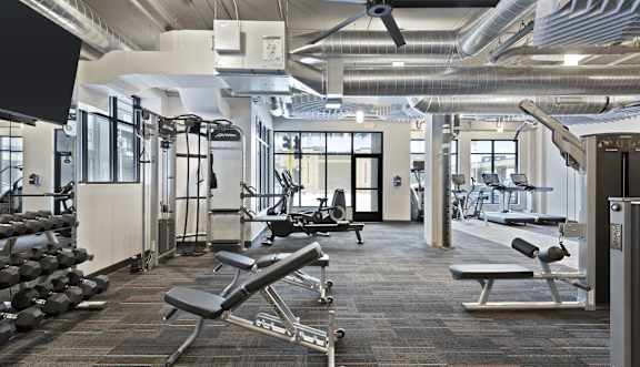 A gym with a variety of equipment including dumbbells, weight machines, and a bench press.