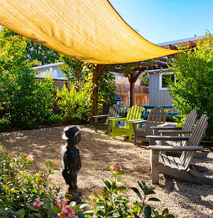 A patio with a yellow shade sail and green chairs.