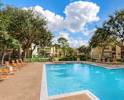 A swimming pool surrounded by trees and chairs.