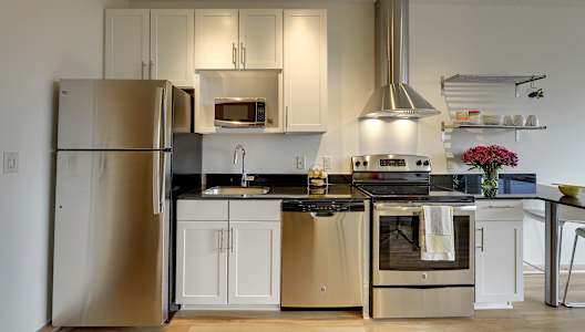 Kitchen with white cabinets, stainless steel appliances, black granite countertop and breakfast nook in the Flat D studio floor plan at Coze Flats
