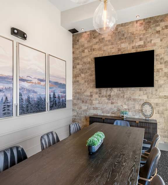 A conference room with a long table and chairs, a flat screen TV, and pictures on the wall.