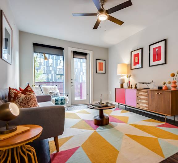 A living room with a grey couch, a yellow table, and a colorful rug.