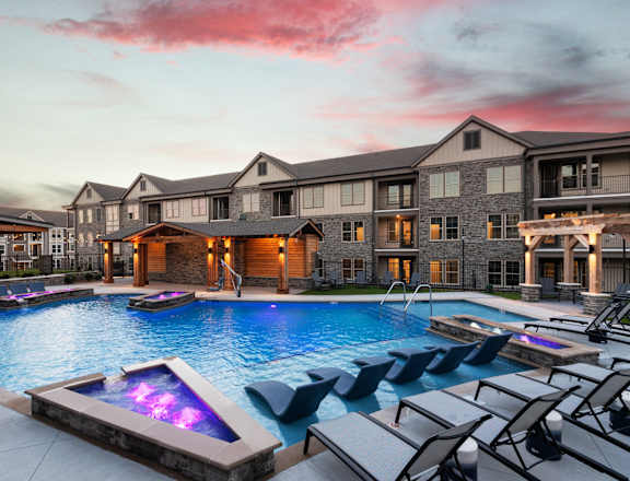 a large swimming pool with lounge chairs in front of an apartment building