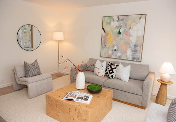 A living room with a grey couch, a wooden coffee table, and a painting on the wall.