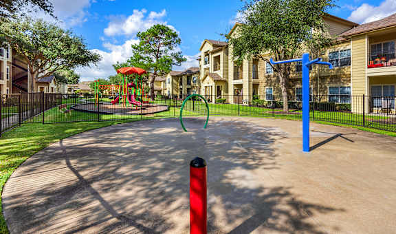 A playground with a red post and a blue pole in the foreground with apartment buildings in the background.