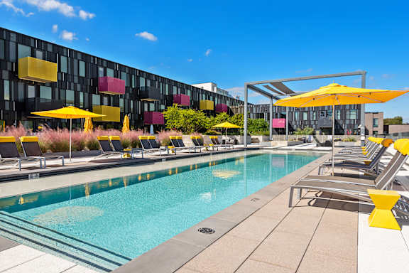 A pool area with yellow umbrellas and a modern building in the background.
