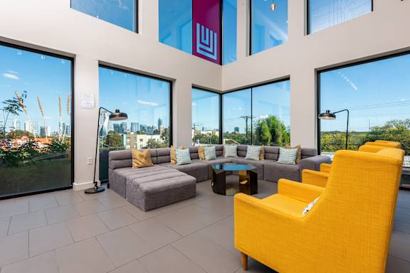 A bright yellow chair is in the foreground of a spacious room with a view of the city.