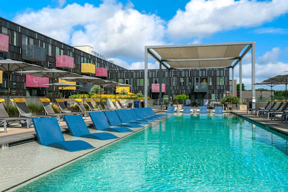 A large swimming pool with blue chairs and a building in the background.