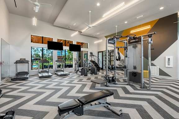 a gym with weights and cardio equipment and a large window