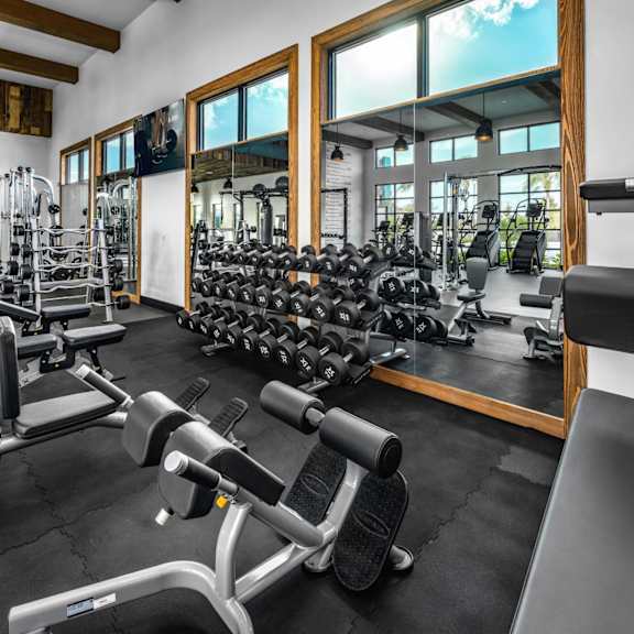 A gym with a variety of equipment including dumbbells, weight machines, and benches.