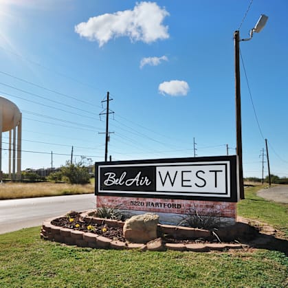 A sign that says "Bellair West" stands in front of a water tower.