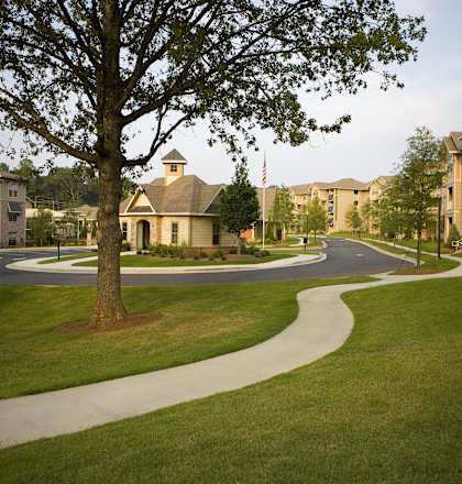 a sidewalk curves through a grassy area with apartment buildings in the background