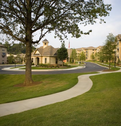 a sidewalk curves through a grassy area with apartment buildings in the background