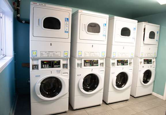 A row of white front load washing machines are lined up in a laundromat.