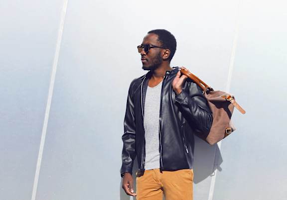 a man wearing a leather jacket and carrying a brown bag