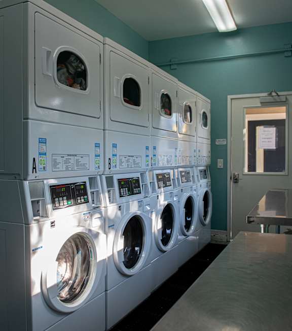 A row of white front loading washing machines are lined up in a laundromat.