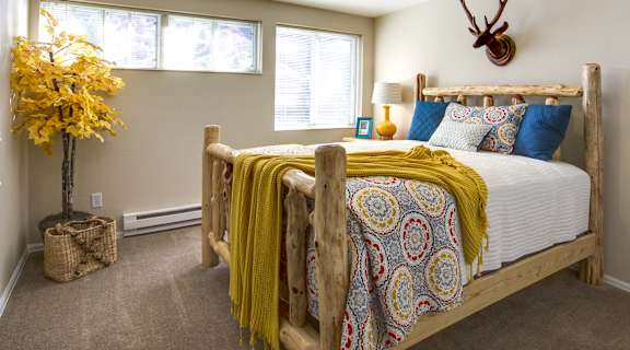 A bedroom with a bed, a yellow blanket, a yellow tree, and a deer head on the wall.