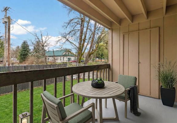 A wooden table with chairs on a patio with a view of a house and trees.