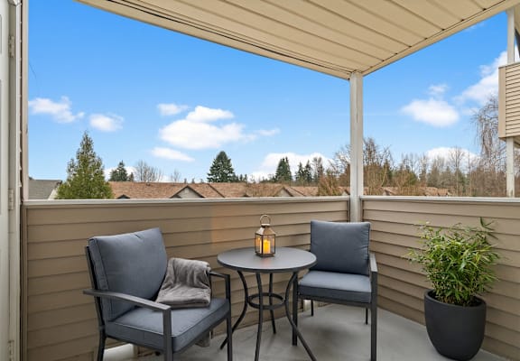A patio with a table and two chairs and a potted plant.