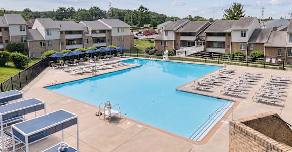 A swimming pool surrounded by sun loungers and apartment buildings.