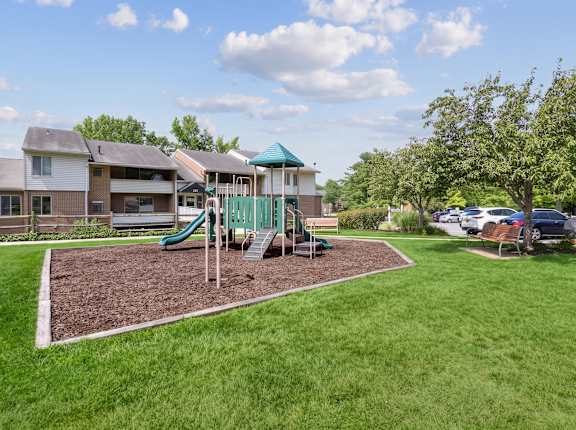 A playground with a green slide and a wooden swing set.