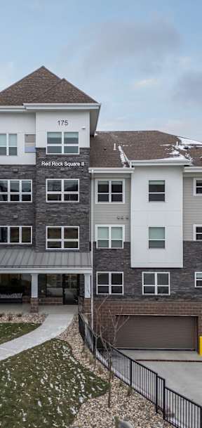 A large multi-story apartment building with a driveway and a small garden in front.