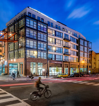 A cyclist is crossing the street in front of a modern multi-story building.